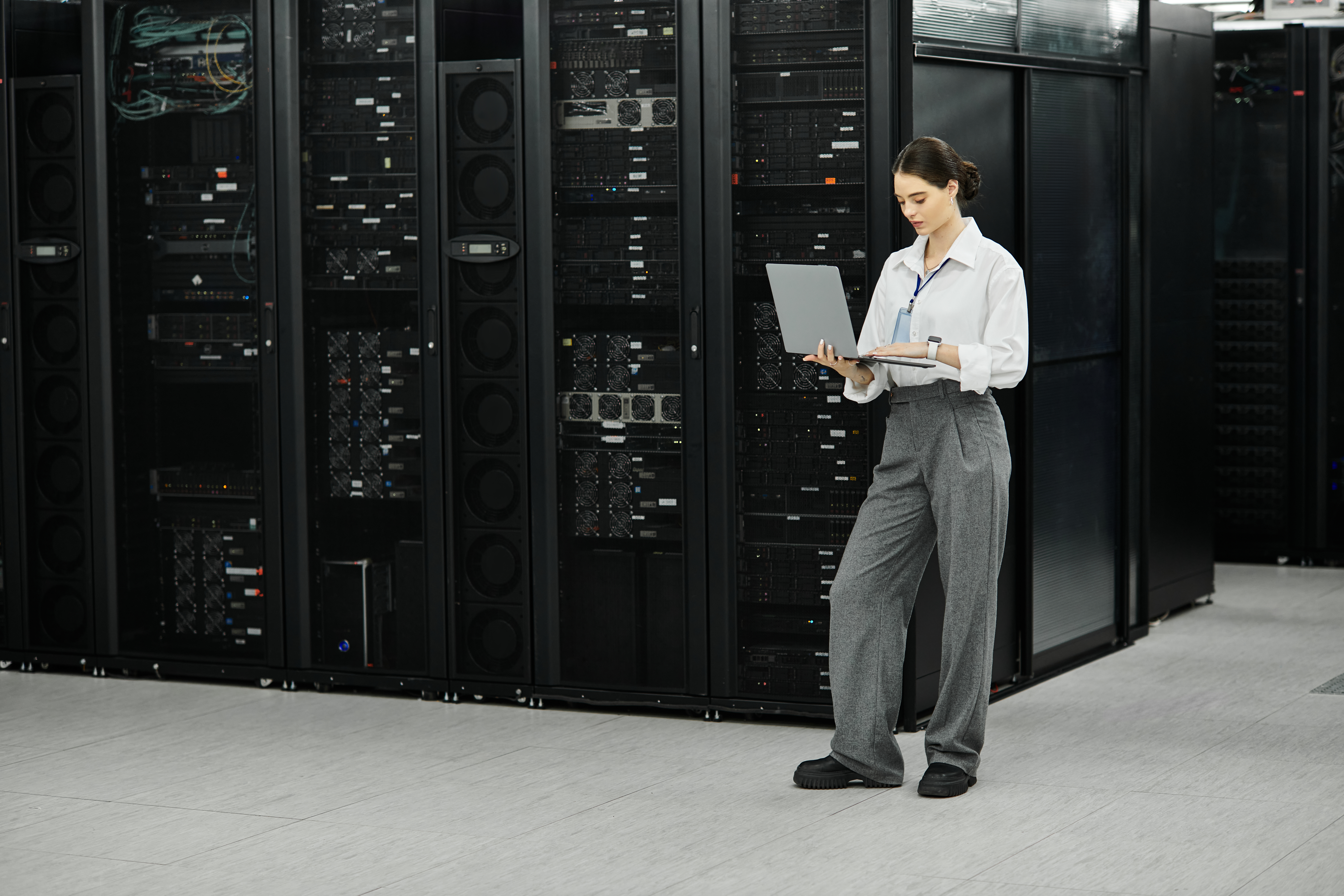 A woman in a white shirt and gray trousers manages server hardware in a data center - Alpha