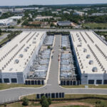 Aerial view of a large warehouse complex with two long white buildings separated by a central road and loading bays in between.
