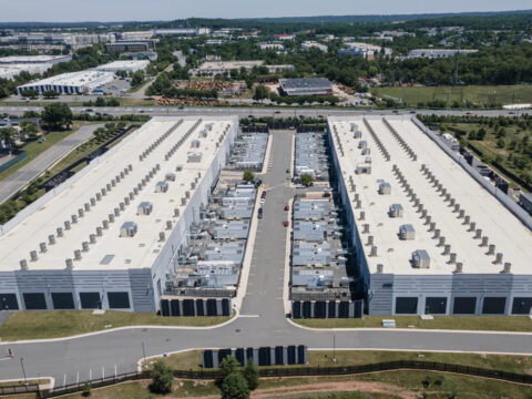 Aerial view of a large warehouse complex with two long white buildings separated by a central road and loading bays in between.