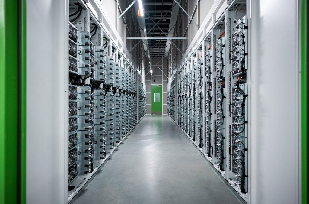Server racks line a data center corridor with cables and a green door at the far end.