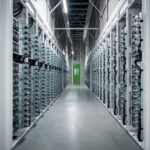 Server racks line a data center corridor with cables and a green door at the far end.