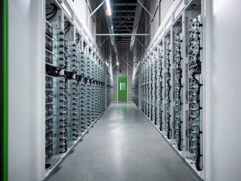 Server racks line a data center corridor with cables and a green door at the far end.