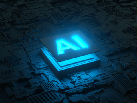 Blue glowing AI symbol atop a dense circuit-board background, representing artificial intelligence technology.