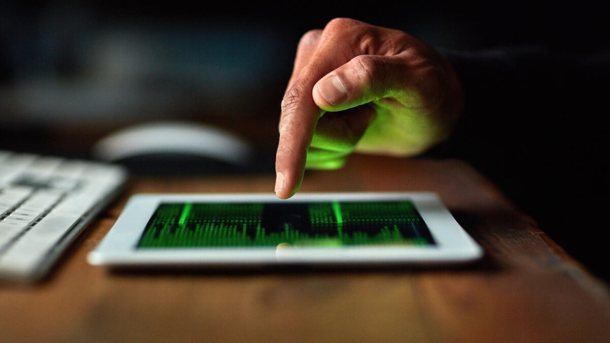 Close-up of a hand tapping a tablet displaying a green data visualization; keyboard blurred in the background.