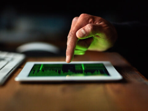 Close-up of a hand tapping a tablet displaying a green data visualization; keyboard blurred in the background.