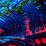 Close-up of network cables and patch panels in a server rack under blue and red lighting, highlighting organized data connections.