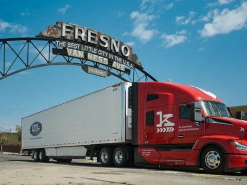 Kodiak_DTL - Alpha Red semi-truck with a white trailer parked under the Fresno arch on a sunny day, foregrounded by a blue sky.