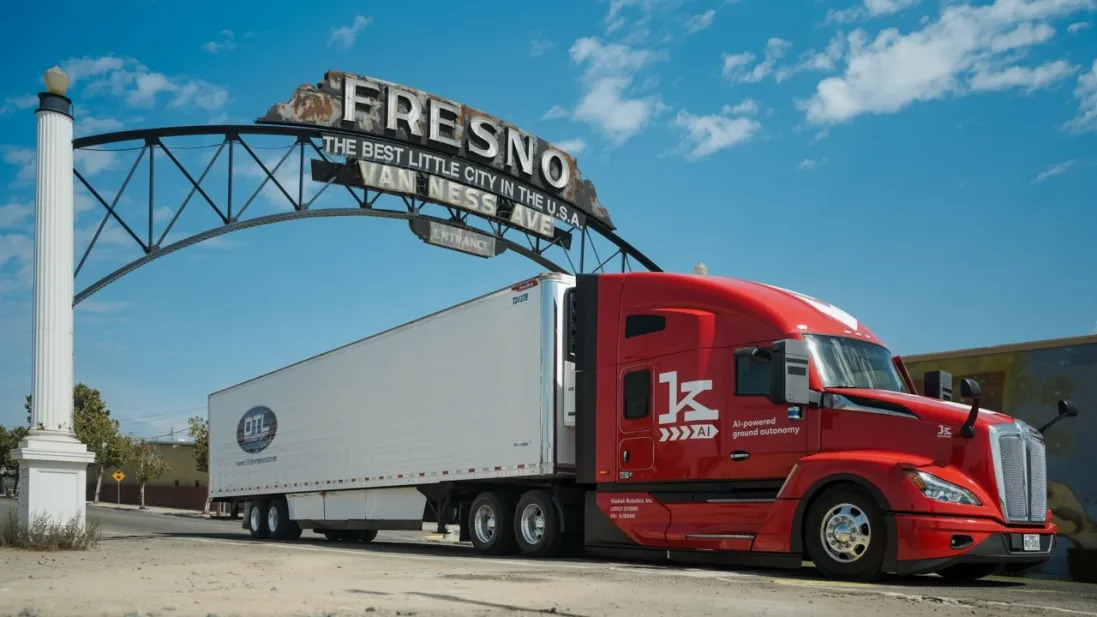 Red semi-truck with a white trailer parked under the Fresno arch on a sunny day, foregrounded by a blue sky.