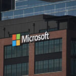 Microsoft logo on a brick office building with glass windows in the foreground.