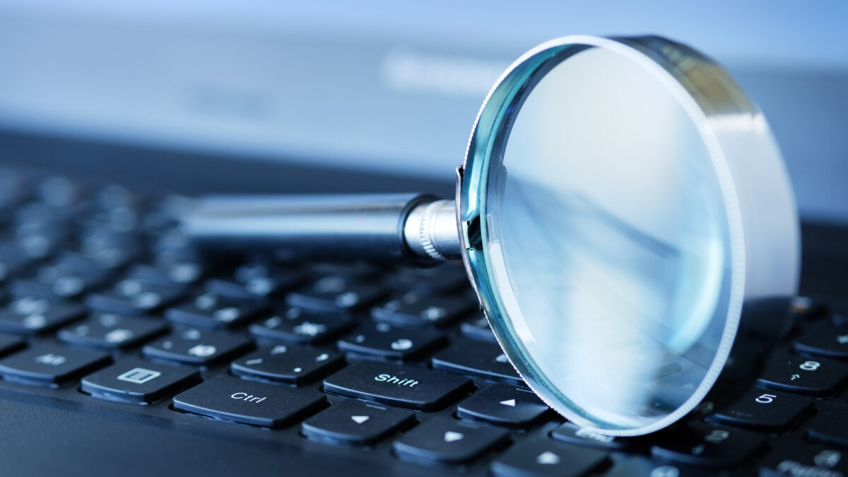 Close-up of a magnifying glass resting on a laptop keyboard, suggesting search or online research.