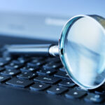 Close-up of a magnifying glass resting on a laptop keyboard, suggesting search or online research.