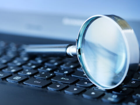 Close-up of a magnifying glass resting on a laptop keyboard, suggesting search or online research.